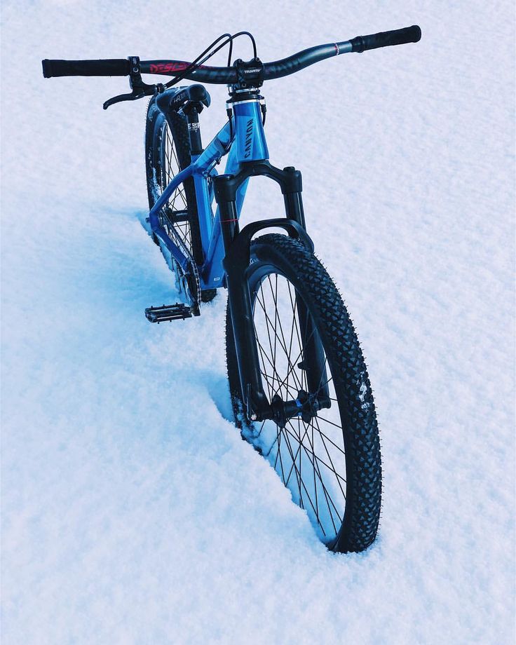 a blue bike parked in the snow on it's front tire and seatpost