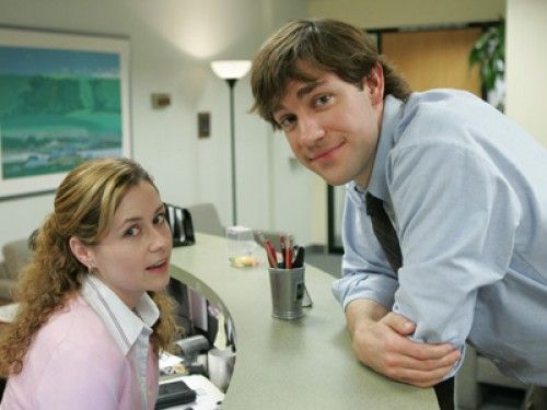 a man standing next to a woman sitting at a desk in an office setting,