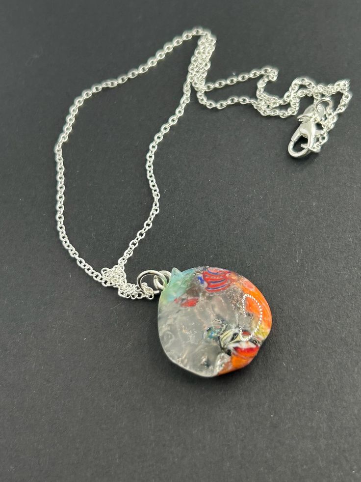 Hand made clear, blue, orange and Millefiori glass pendant on a silver plated 18 Inch chain.  This is a one of a kind beauty. Unique Iridescent Nickel-free Necklace, Artistic Glass Necklace With Round Pendant, Artistic Glass Round Pendant Necklaces, Artistic Glass Round Pendant Necklace, Iridescent Glass Necklaces As Gifts, Artsy Nickel-free Pendant Necklace, Silver Glass Flower Pendant Jewelry, Silver Glass Necklace With Lobster Clasp, Artsy Silver Jewelry With Large Pendant