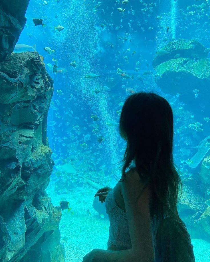 a woman standing in front of an aquarium looking at fish