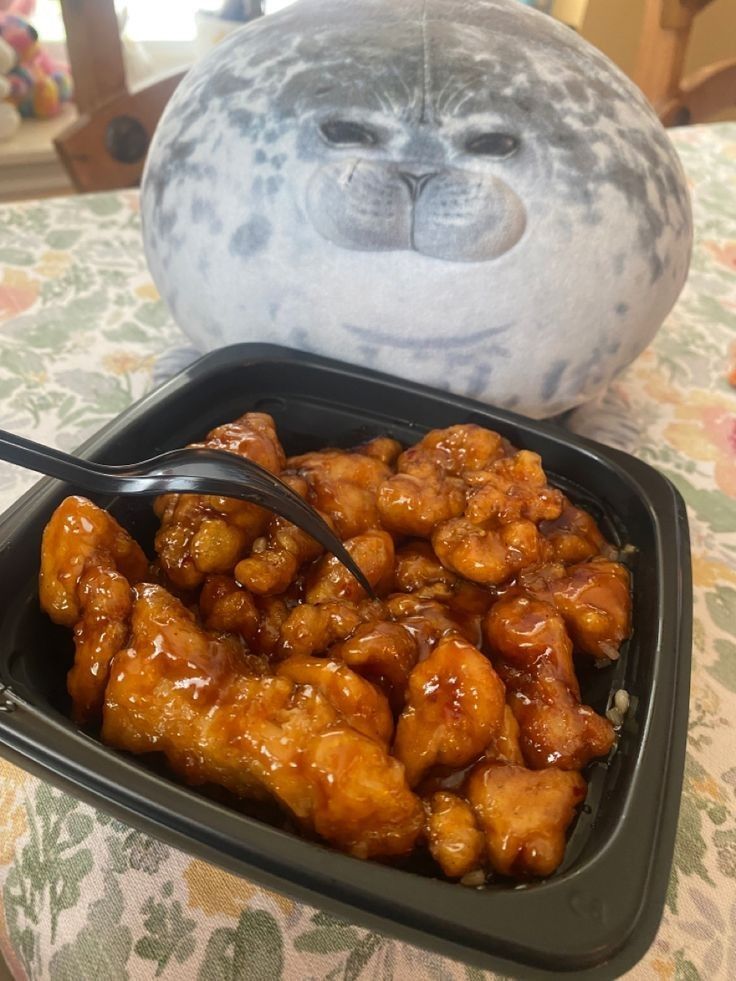 a bowl filled with chicken and sauce next to a stuffed animal on top of a table