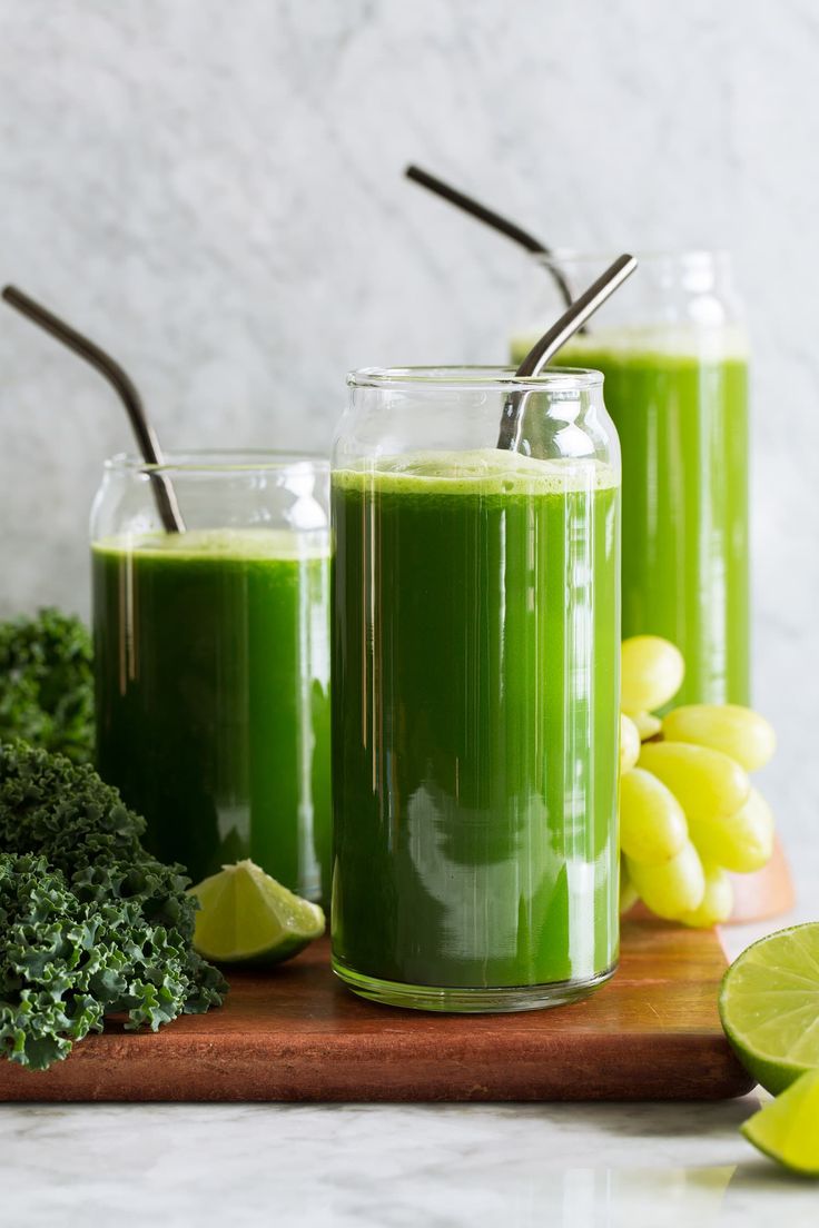 two glasses filled with green smoothie on top of a cutting board