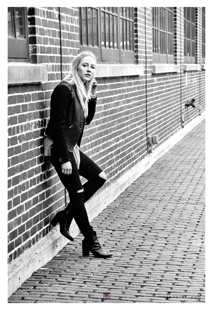 a woman leaning against a brick wall with her hand on her chin and looking at the camera