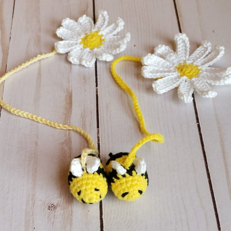 two crocheted flowers are attached to a string on a wooden surface with yarn