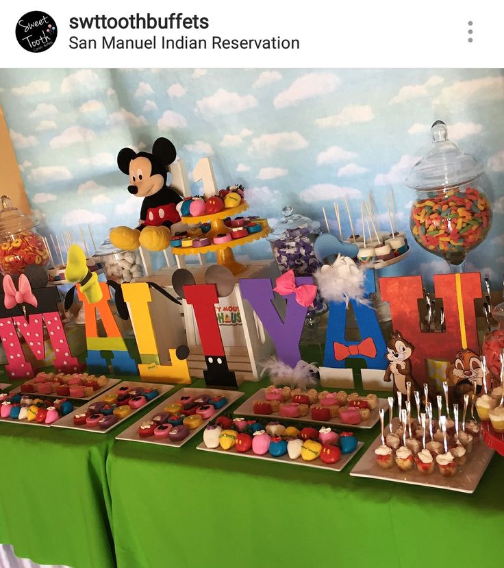 a table topped with lots of cupcakes and cakes next to a mickey mouse sign