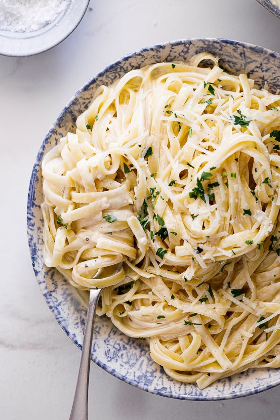 a bowl filled with pasta and parsley on top of a white tablecloth next to two bowls of food