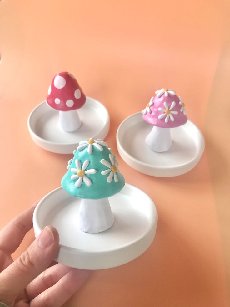 three miniature mushrooms sitting on top of white plates with pink, blue and green tops