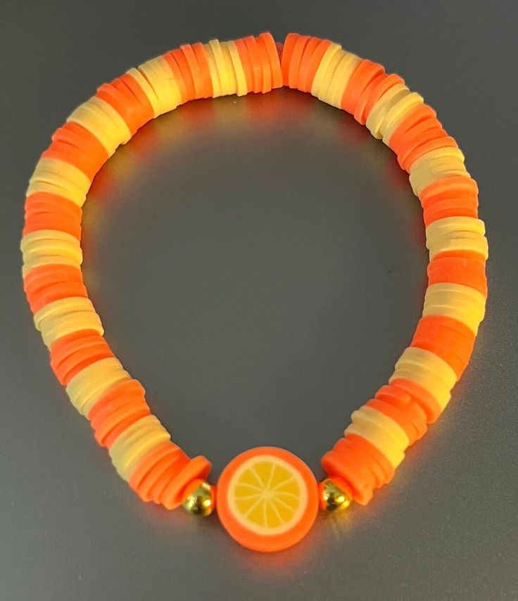 an orange, yellow and white bracelet with gold beads on a gray surface is shown