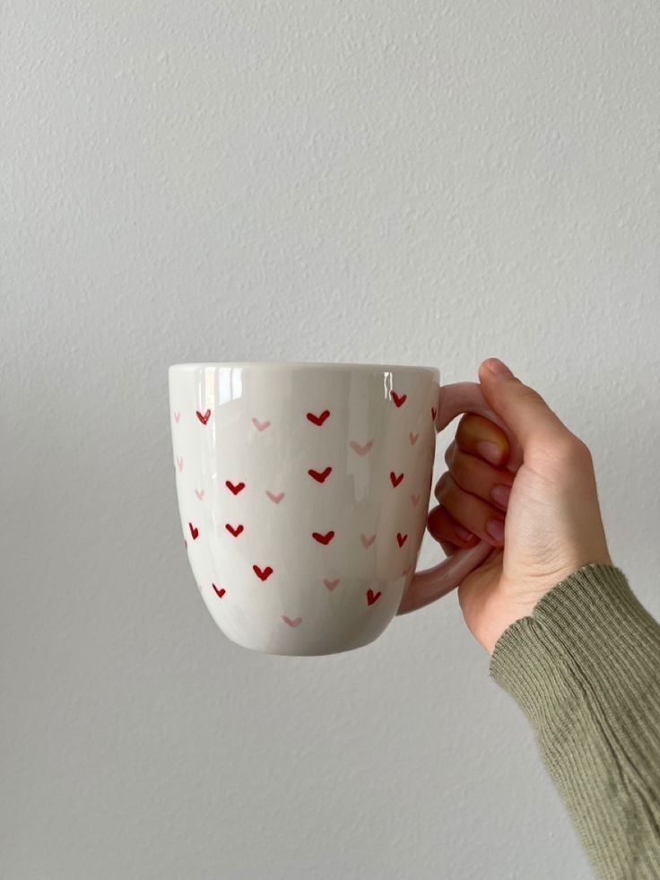 a person is holding a coffee cup with hearts painted on the outside and inside, in front of a white wall