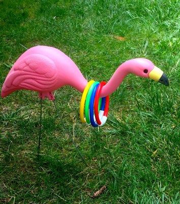 a pink flamingo toy with multi colored bands on it's neck standing in the grass