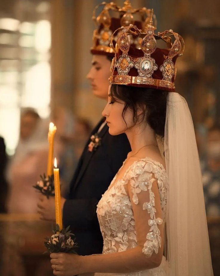 a woman wearing a tiara and holding a candle in her hand while standing next to a man