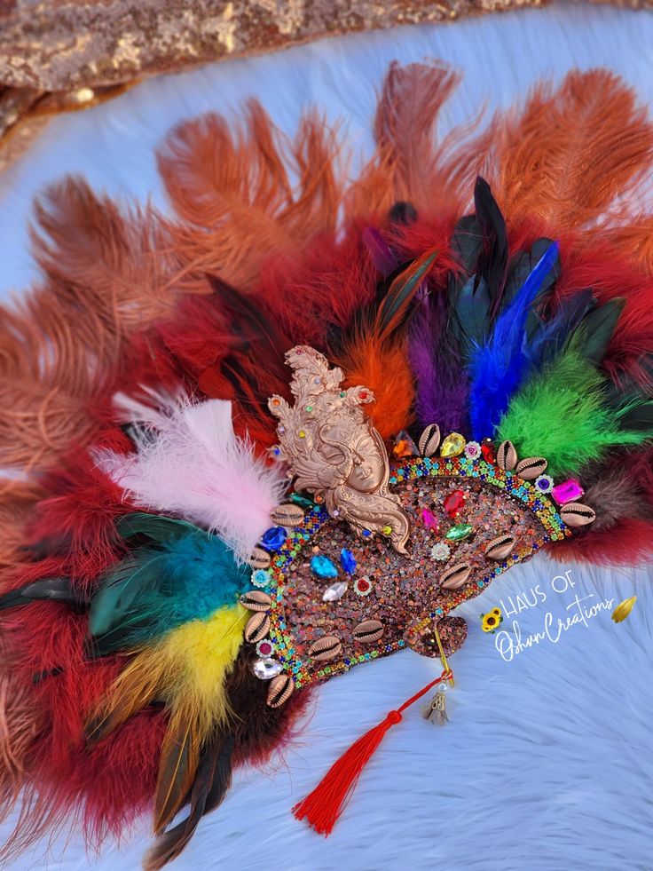 Oya inspired hand fan with 9 color feathers, brown ostrich feathers, mask mould, cowrie shells & jewels. Each item is respectfully made with the highest quality materials. Please note: All items are made to order and ship within 4-6 weeks! Style may slightly vary due to material availability. For custom color or style, you may ... Bohemian Headpieces For Carnival And Festivals, Bohemian Multicolor Headpieces For Carnival, Traditional Handmade Headpieces For Carnival, Traditional Handmade Carnival Headpieces, Djembe Drum, Cowrie Shells, Ostrich Feathers, Cowrie Shell, Hand Fan