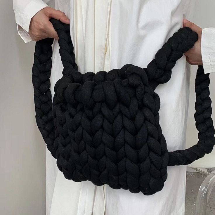 a woman is holding a black bag made out of yarn