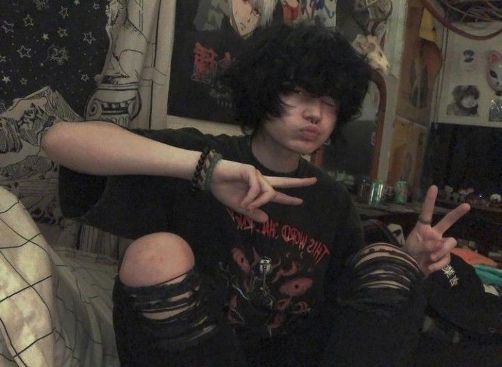 a young man with black hair sitting on a couch making the peace sign while holding his hand up