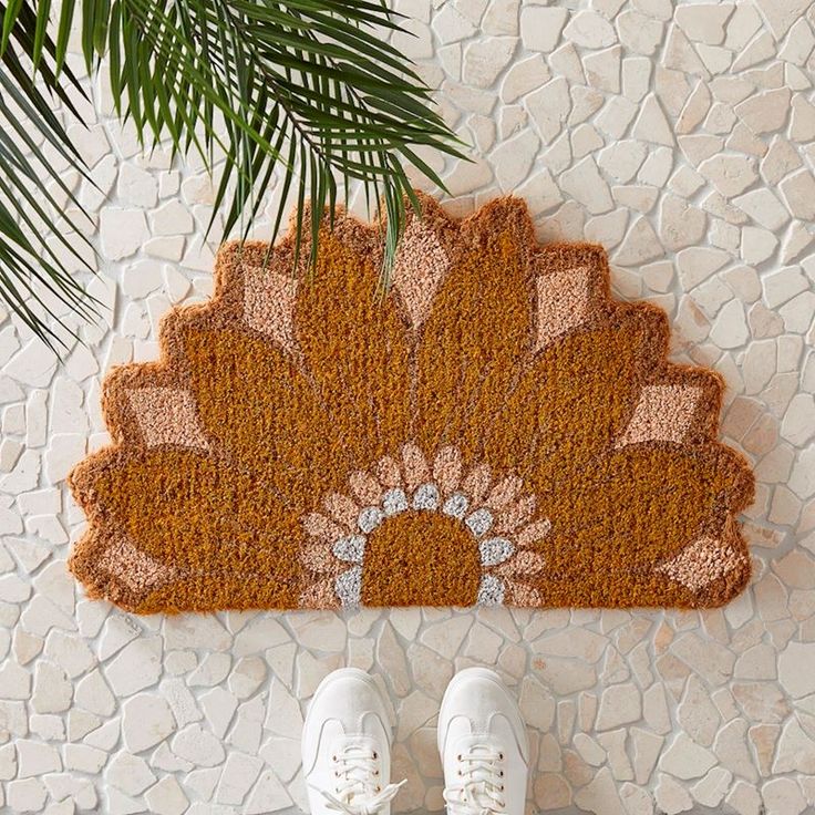 a pair of white shoes standing in front of a door mat with a flower design