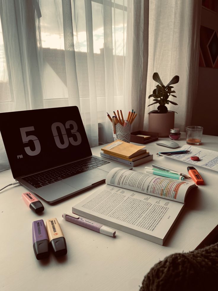 an open laptop computer sitting on top of a desk next to books and pencils