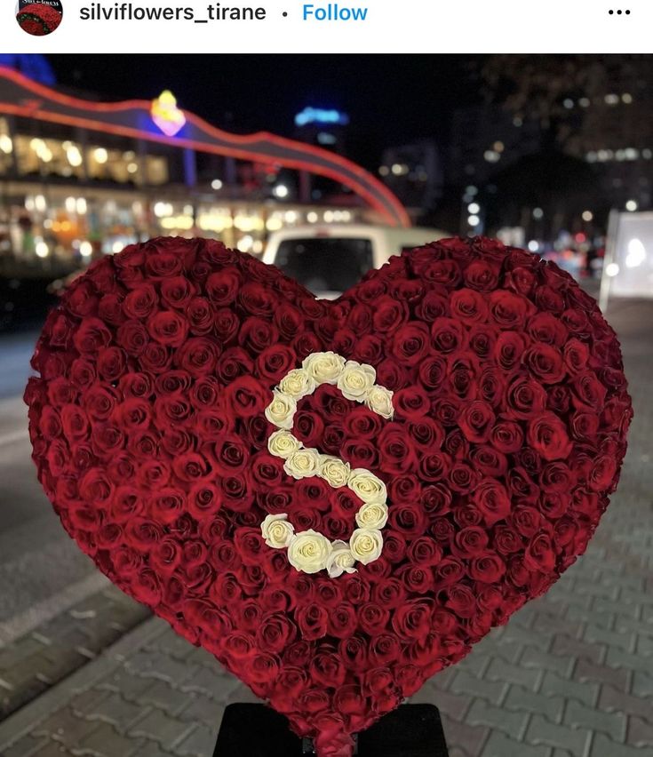 a heart shaped arrangement with the letter s made out of red and white roses in front of a city street