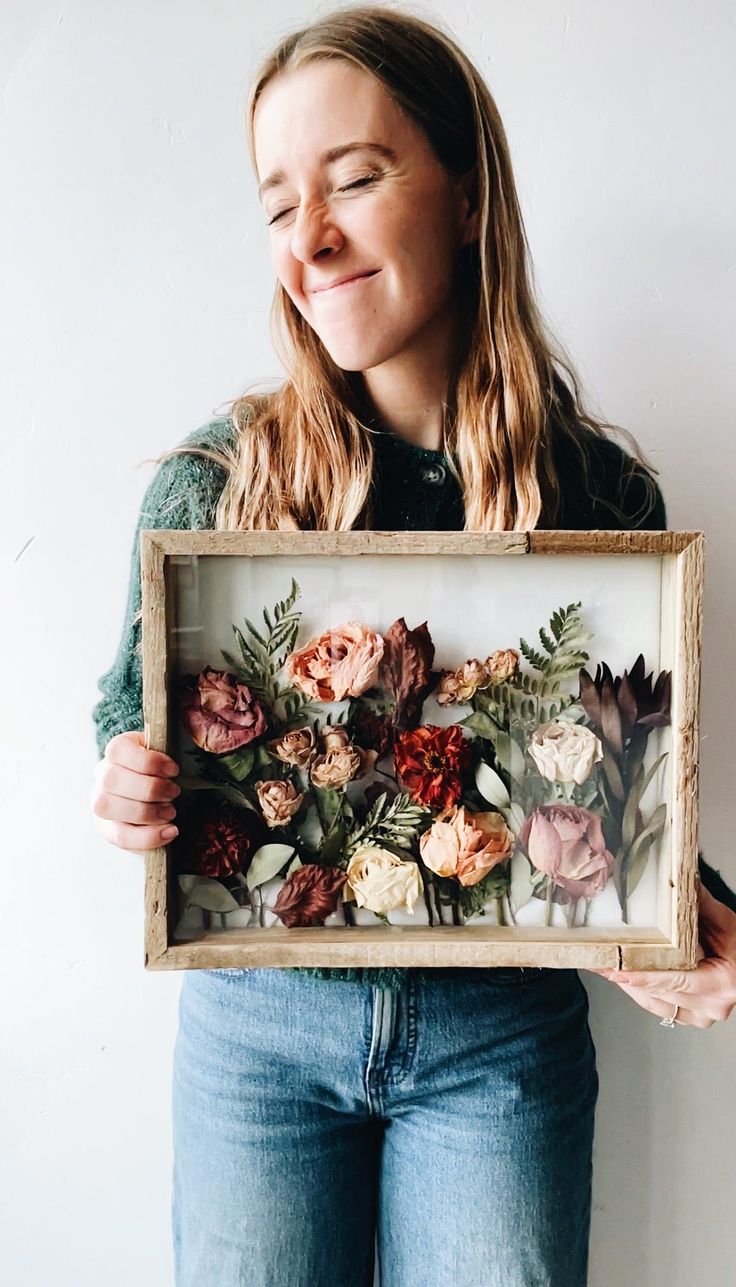 a woman holding up a framed painting with flowers on it