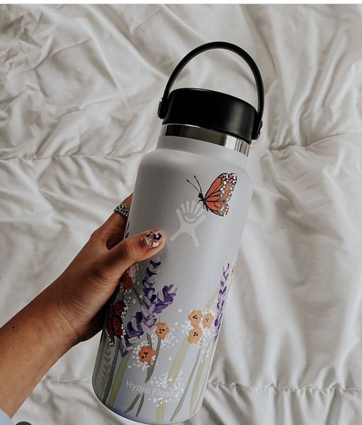 a hand holding a white water bottle with butterflies on it and flowers in the background