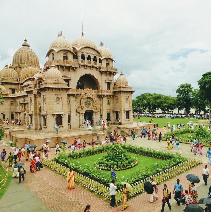 many people are walking around in front of a building with an elaborate lawn and flower garden