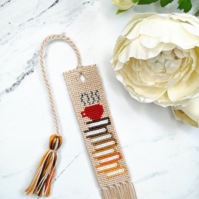 a cross stitch bookmark next to a white flower on a marble table with flowers in the background