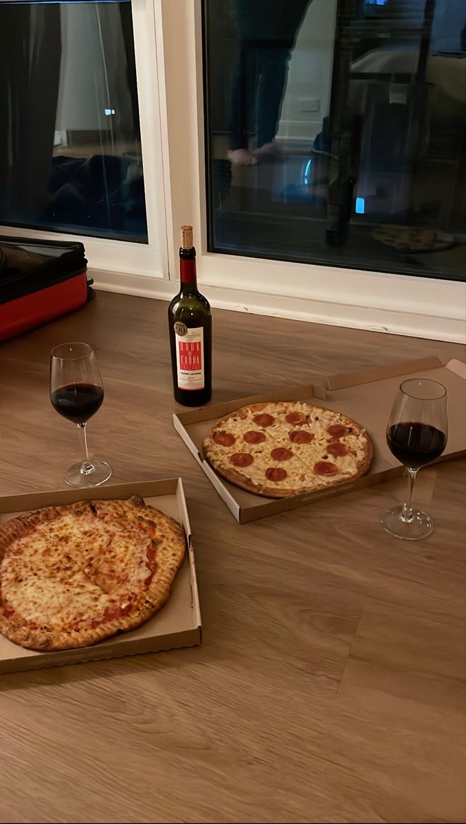 two pizzas sitting on top of cardboard boxes next to wine glasses and a bottle