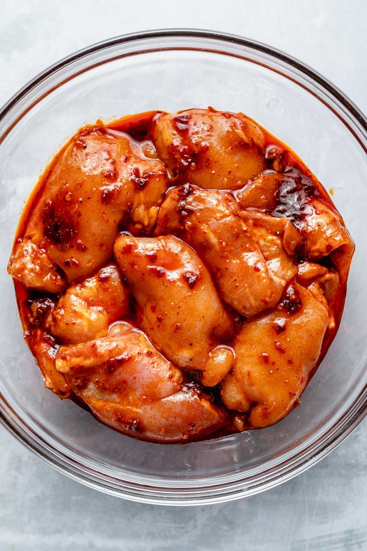 a glass bowl filled with chicken wings covered in sauce on top of a white table