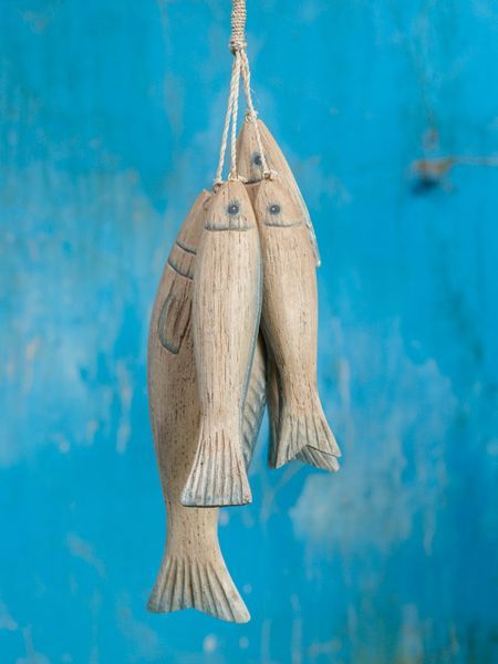 two wooden fish hanging from strings against a blue wall