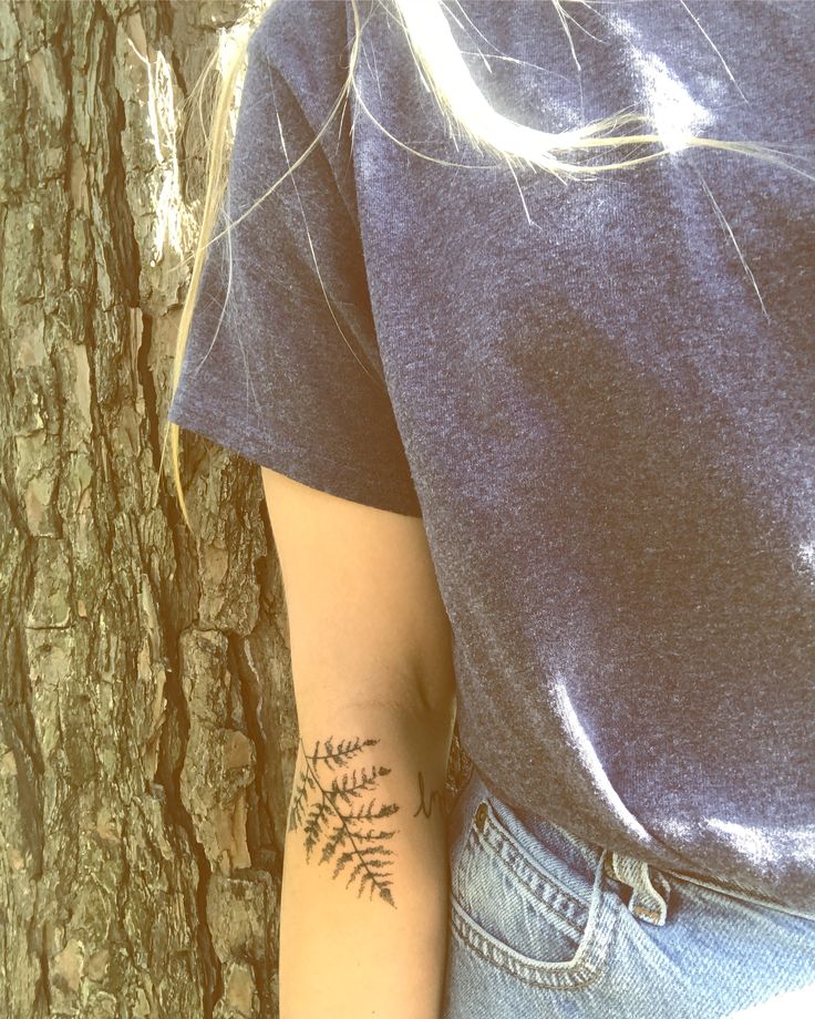 a woman with a tattoo on her arm next to a tree