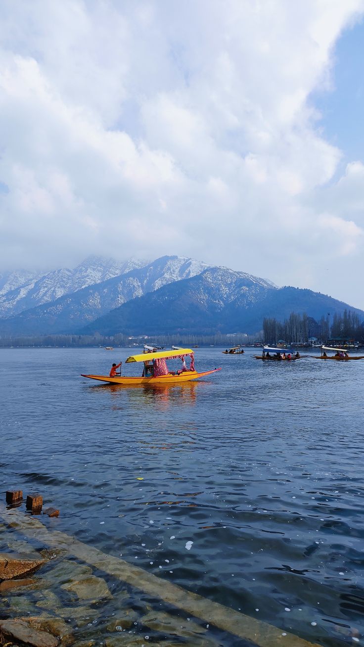 a yellow boat floating on top of a lake next to snow covered mountain range in the distance