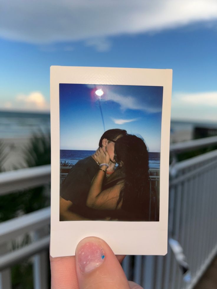 a person holding up a polaroid photo with the ocean in the background