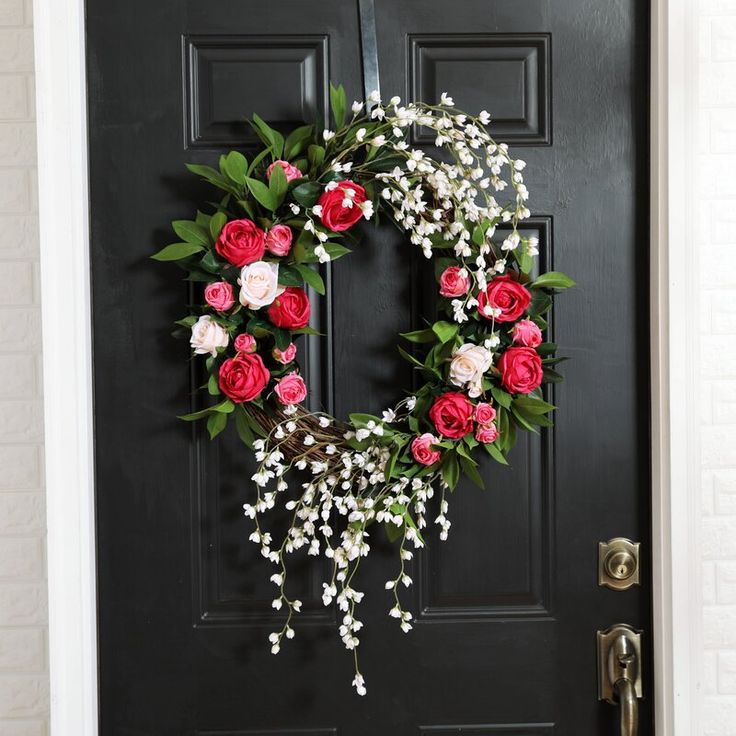 a wreath on the front door with red and white flowers hanging from it's side