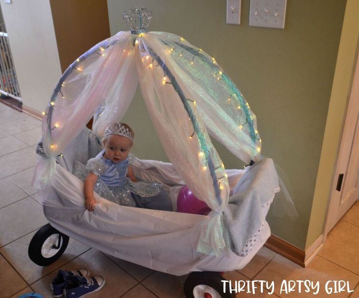 a baby sitting in a toy carriage with fairy lights on the roof and canopy over it's head