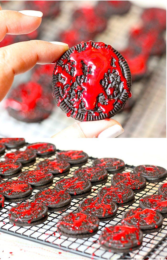 a person holding up a cookie with red icing on it next to a cooling rack full of cookies