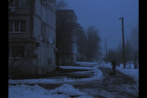 a person walking down a snowy street in front of tall buildings on a dark, overcast day