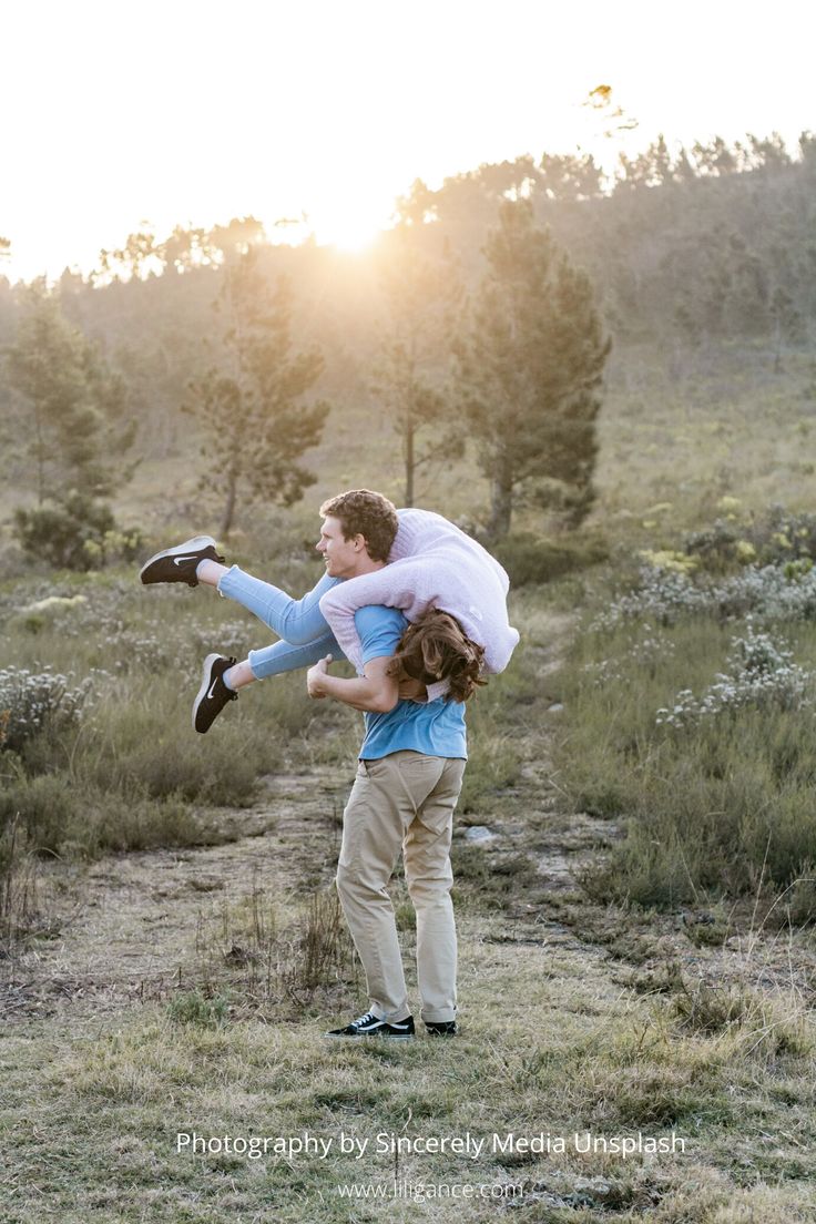 a man carrying a woman on his back in the middle of a field at sunset