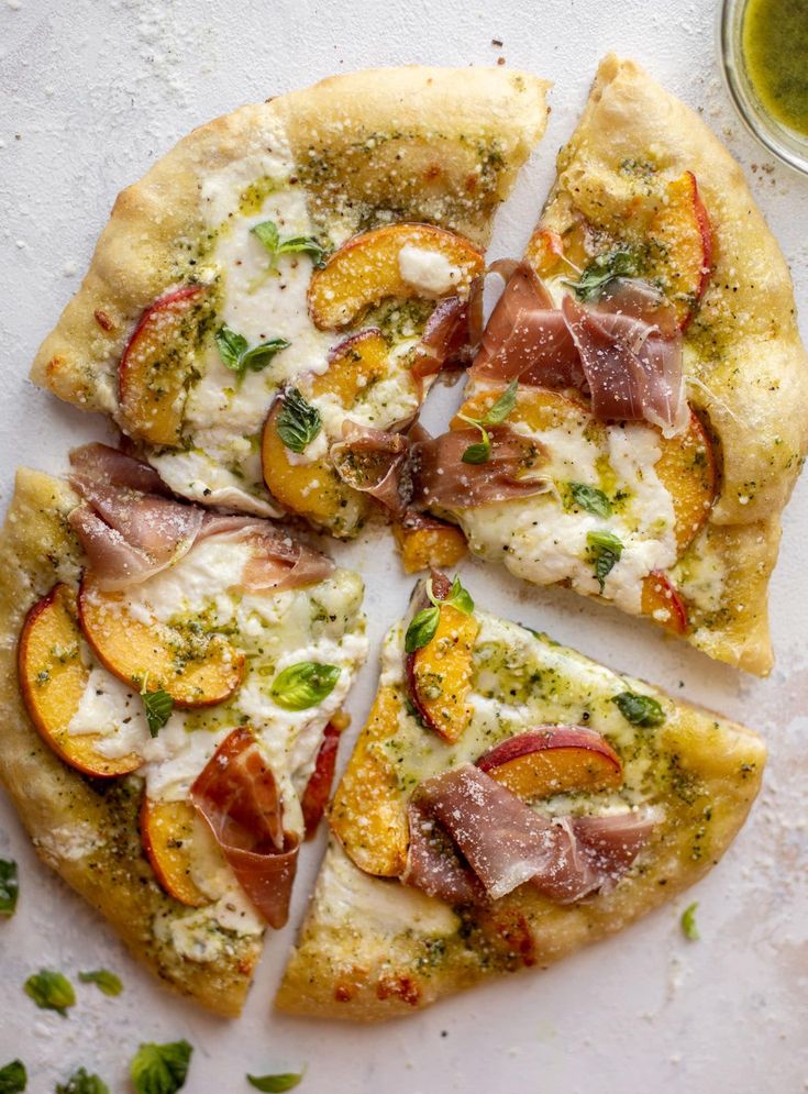 a pizza with different toppings cut into slices on a white surface next to a glass of olive oil