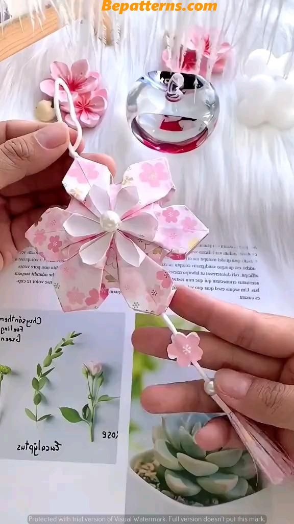 two hands are holding small flowers on top of an open book, and another hand is holding a card