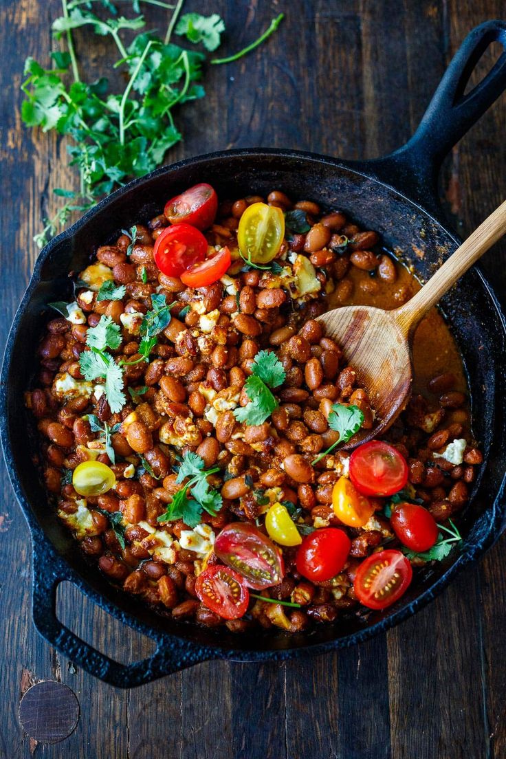 a skillet filled with beans, tomatoes and parsley on top of a wooden table