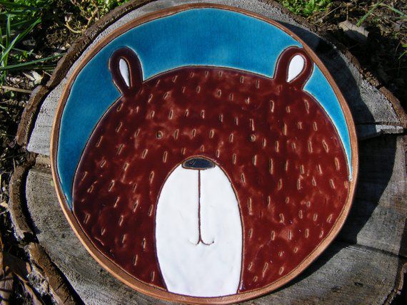 a plate with a bear painted on it sitting on top of a tree stump in the grass