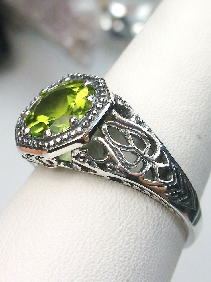 Natural Peridot RingNew Vic Design#D11 Inspired by Victorian and Edwardian designs, this stunning antique reproduction ring is crafted in white gold. This gorgeous ring is set with a flawless round natural peridot. The stunning gemstone is 8mm in diameter. The band is marked 925 (sterling silver),10k or 14k as chosen. Notice the beautifully intricate design of the silver filigree setting and band. The delicate swirl filigree craftsmanship travels down the band and morphs into angular accents. Th Classic Peridot Jewelry With Prong Setting, Classic Peridot Jewelry With Accent Stones, Vintage Green Rings With Accent Stones, Classic Peridot Ring Jewelry, Antique Green Rings With Prong Setting, Classic Peridot Green Rings, Classic Green Peridot Ring, Green Rings With Intricate Design For Promise, Green Promise Ring With Intricate Design