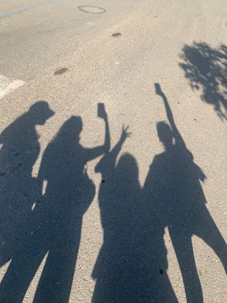 three people are standing in the street with their shadows on the ground and one person is holding a baseball bat