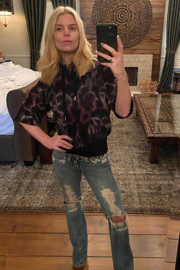 a woman taking a selfie with her cell phone in front of the camera and wearing ripped jeans