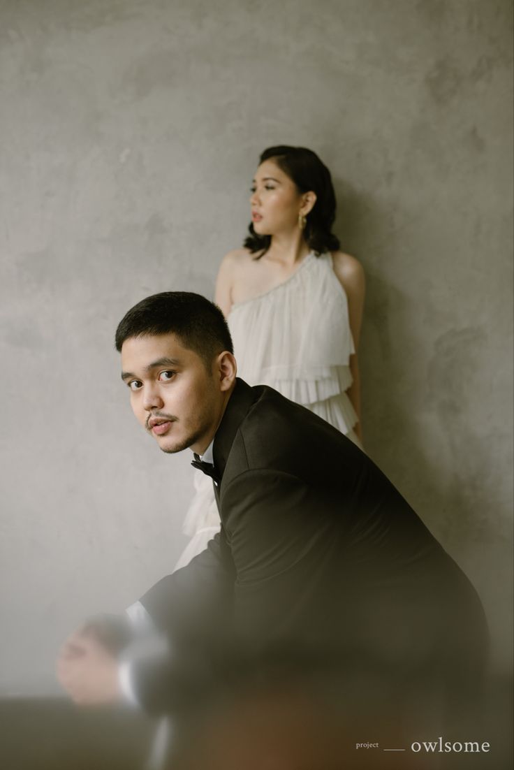 a man and woman standing next to each other in front of a gray wall,