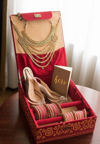 an open red box with gold jewelry and shoes in it sitting on a table next to a window