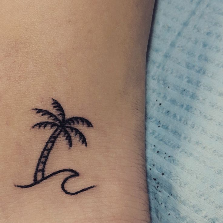 a small palm tree on the wrist tattoo is shown in black ink with waves coming up from it