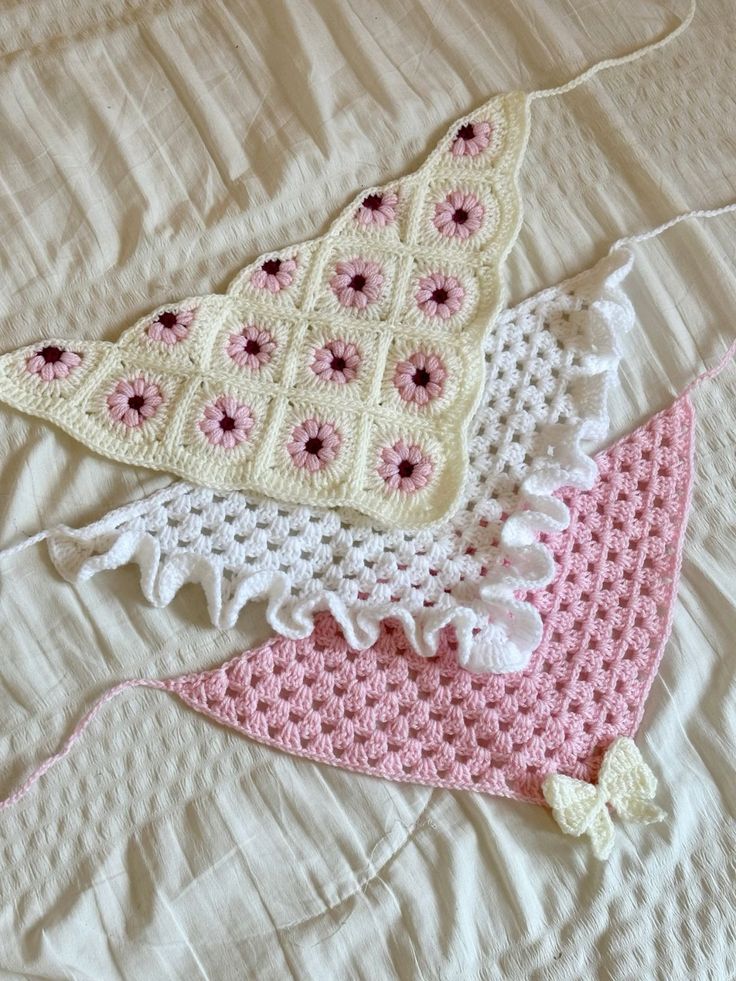 three crocheted items laying on top of a white bed sheet with pink flowers