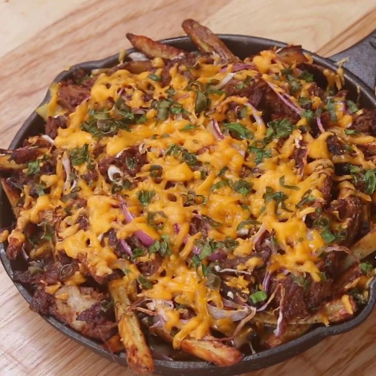 a skillet filled with meat and cheese on top of a wooden table