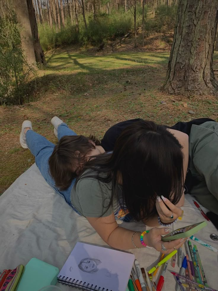 two people laying on a blanket in the woods with their back to each other and writing