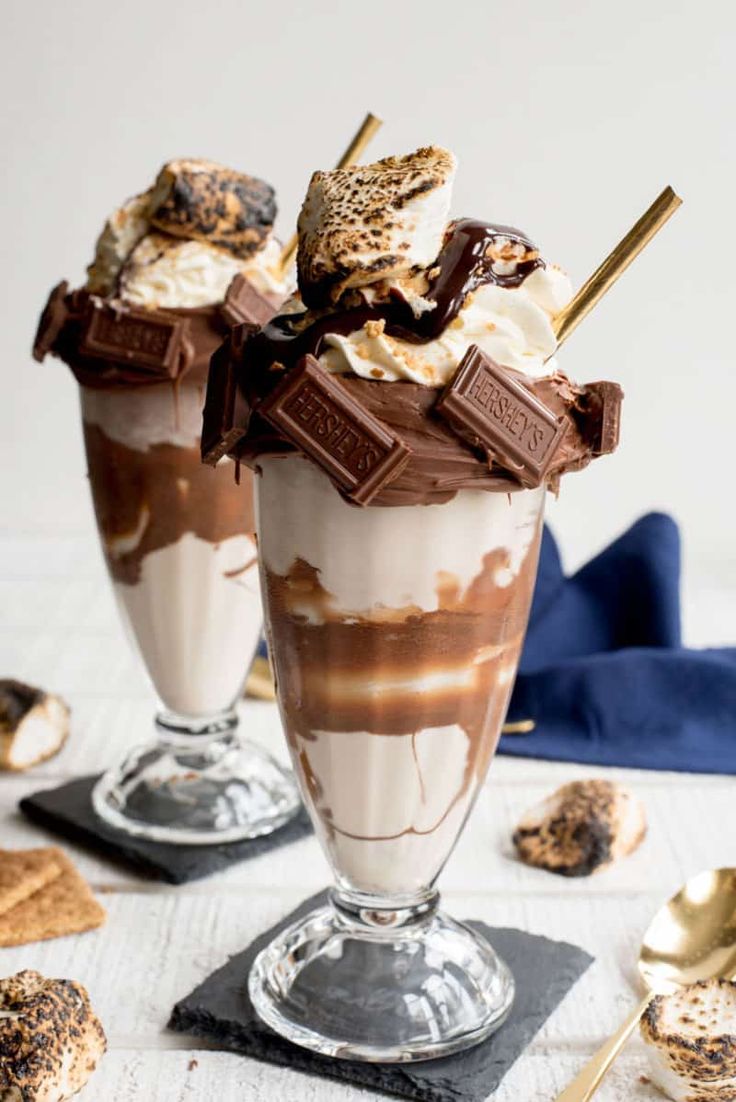 two glasses filled with ice cream and toppings on top of a white tablecloth